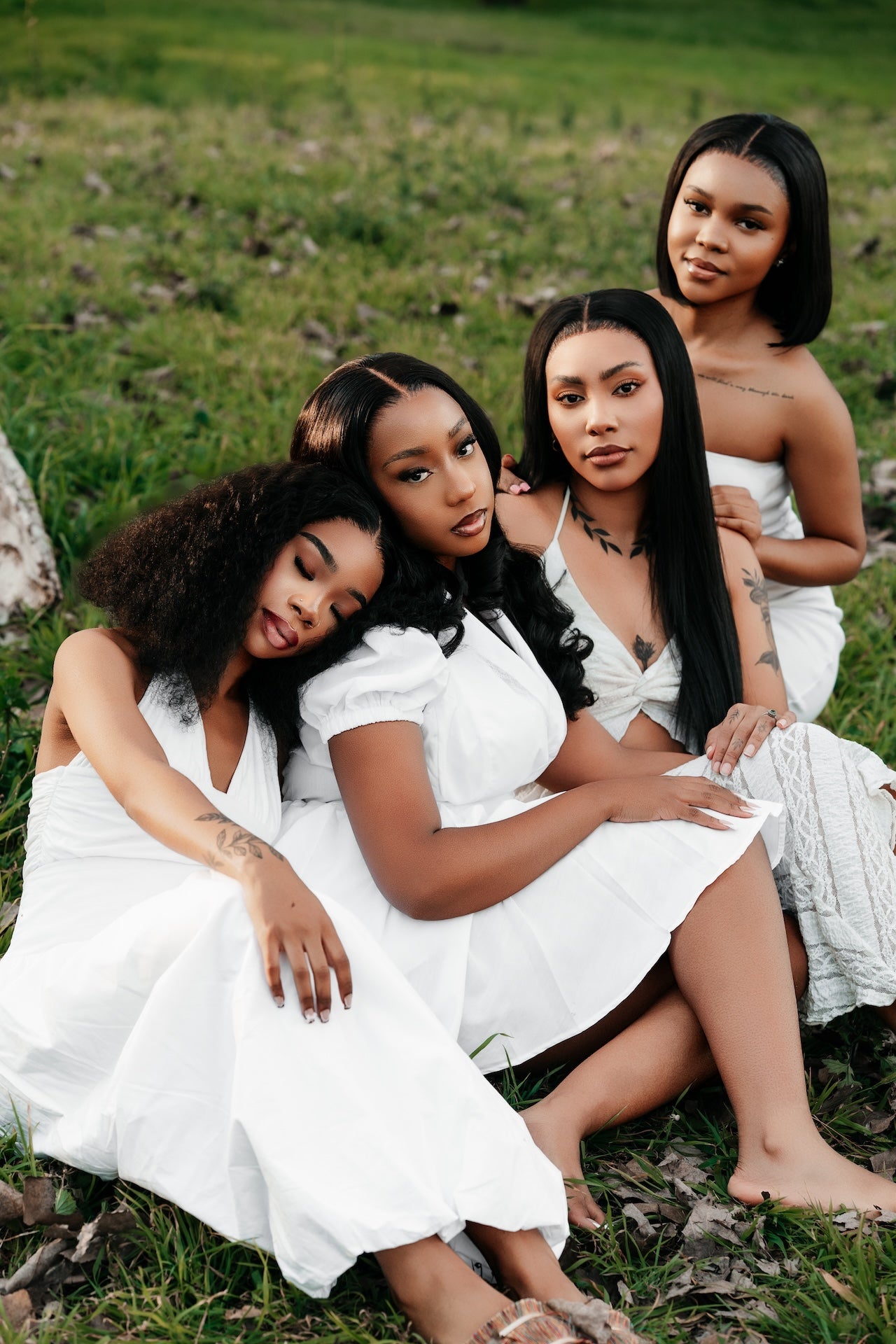 Four women in white dresses sitting on a grassy field